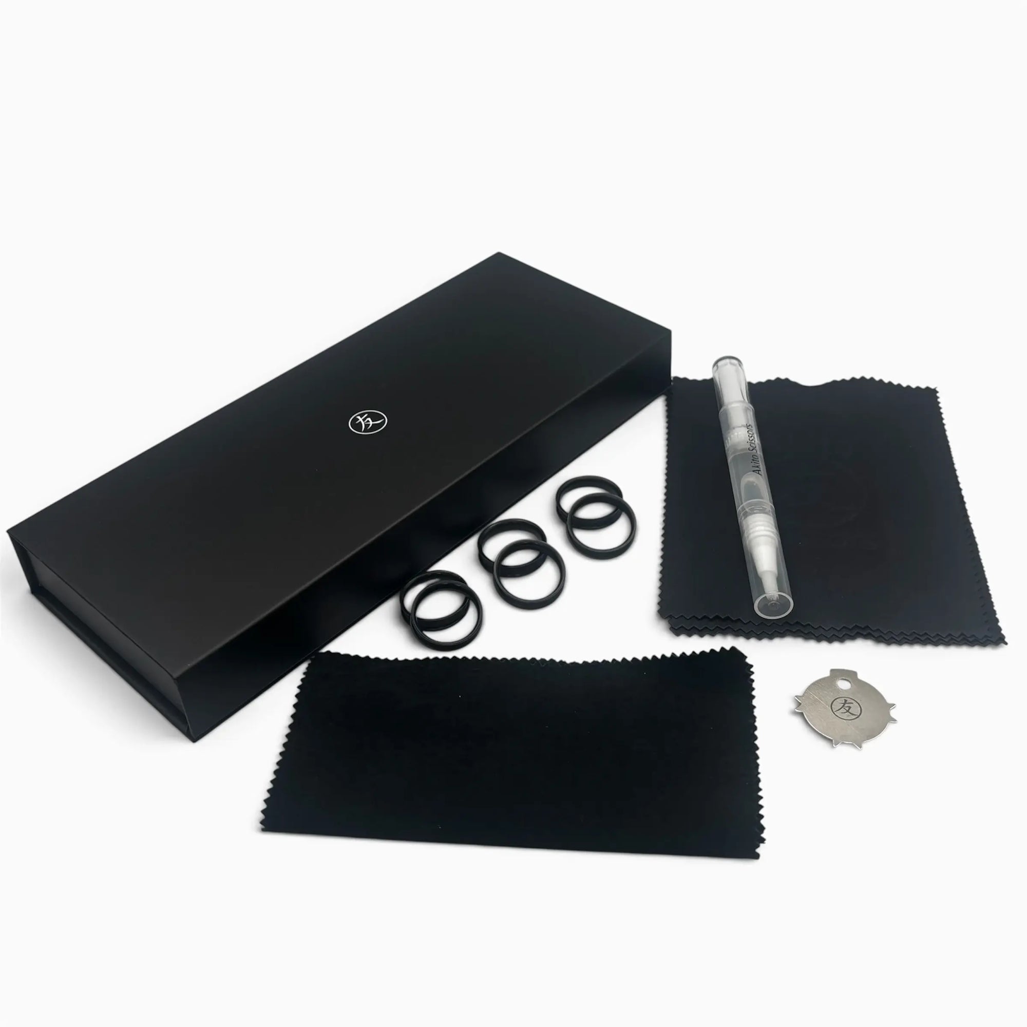 A black presentation box with a small circular logo, shown with several black accessory pieces and two black microfiber cloths on a light gray background. A clear cylindrical component with a silver-toned end is also visible.
