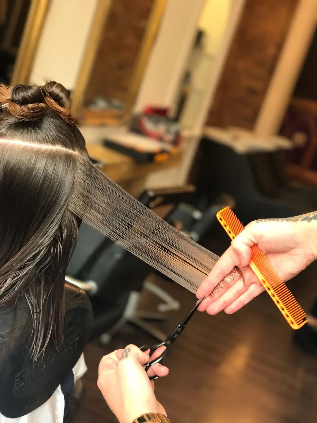 Hairdresser cutting a customer's hair with scissors and a comb in a salon setting.