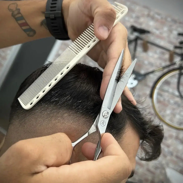 Person cutting hair with scissors and a comb in a close-up shot.