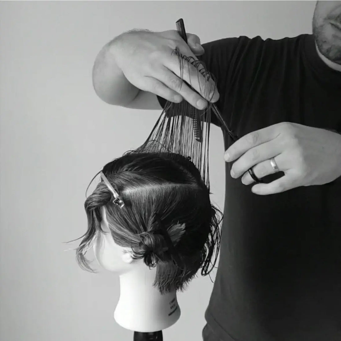 Person cutting hair on a mannequin head using Akito scissors with a brush and comb.